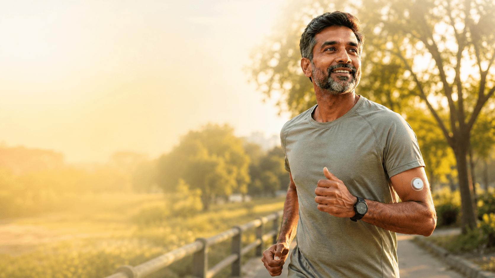 A smiling man jogging outdoors with a continuous glucose monitor on his arm